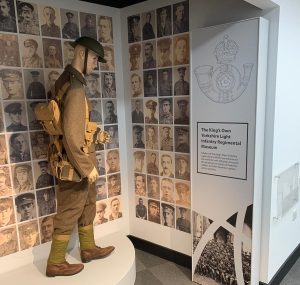 Photograph of a soldier mannequin surrounded by walls featuring black and white photographs of soldiers' faces