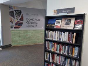 photo showing bookcase with book and graphic on wall reading welcome to doncaster central library