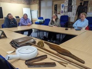 A group of adults looking at a selection of artefacts from the museum collection.