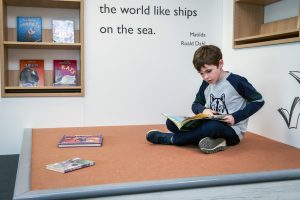 A child sat with his legs crossed, reading a book.