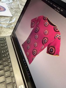 A laptop displaying a pink t-shirt with pastel coloured roundels.
